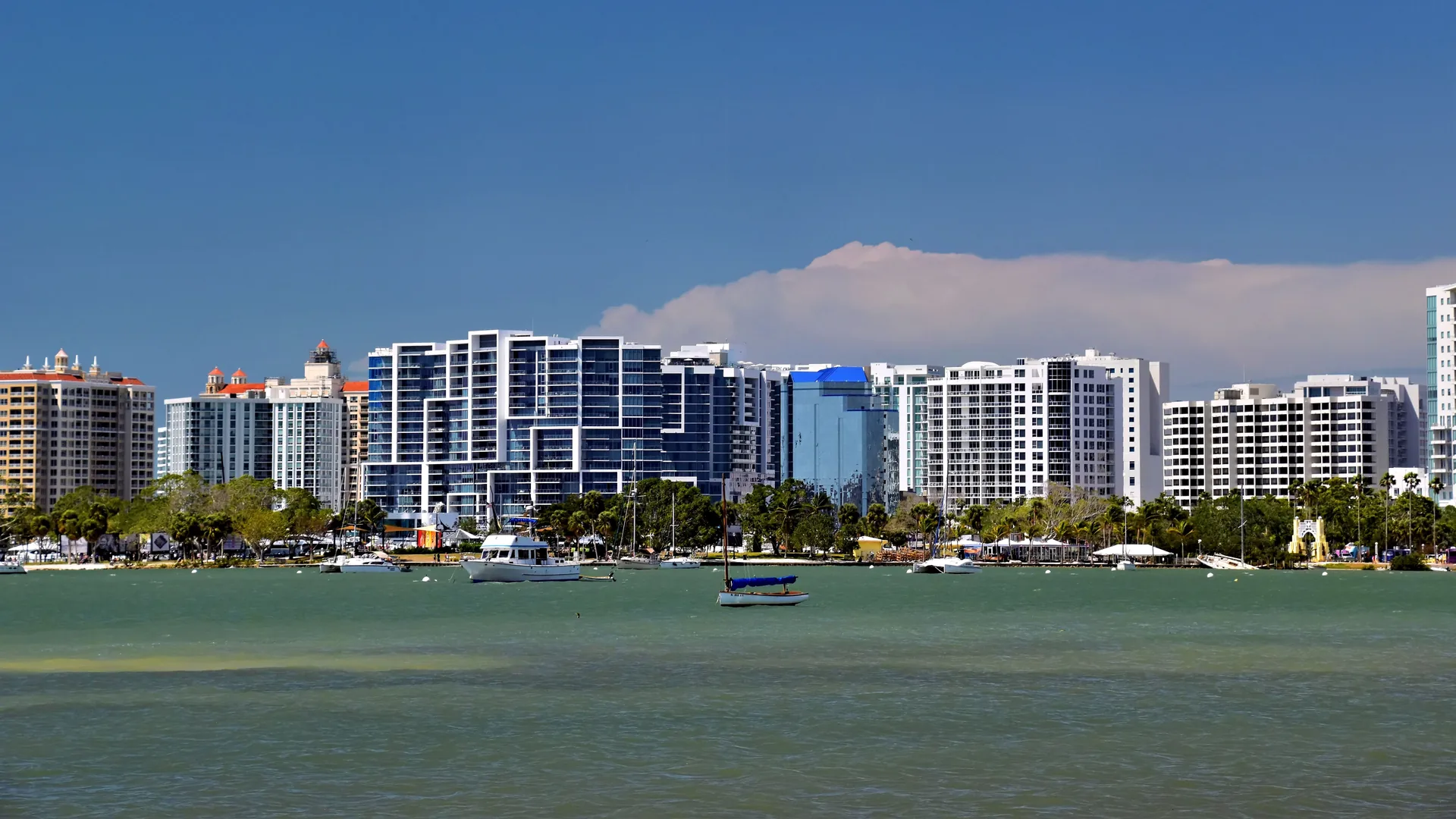 The Sarasota bayfront skyline of mid-rise condominium towers across the water, with sailboats moored in the bay